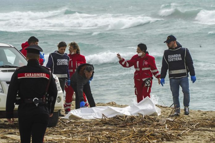 Voluntarios de la Cruz Roja italiana y personal del servicio de guardacostas recuperan un cadáver el domingo 26 de febrero de 2023 luego de que un bote con migrantes se partió en un mar agitado, en una playa cerca de Cutro, en el sur de Italia. (Antonino Durso/LaPresse vía AP)