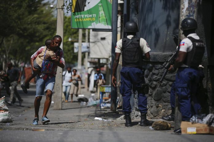 ARCHIVO - Un padre corre con su hijo frente a agentes de la policía, el 3 de marzo de 2023, en Puerto Príncipe, Haití. (AP Foto/Odelyn Joseph, archivo)